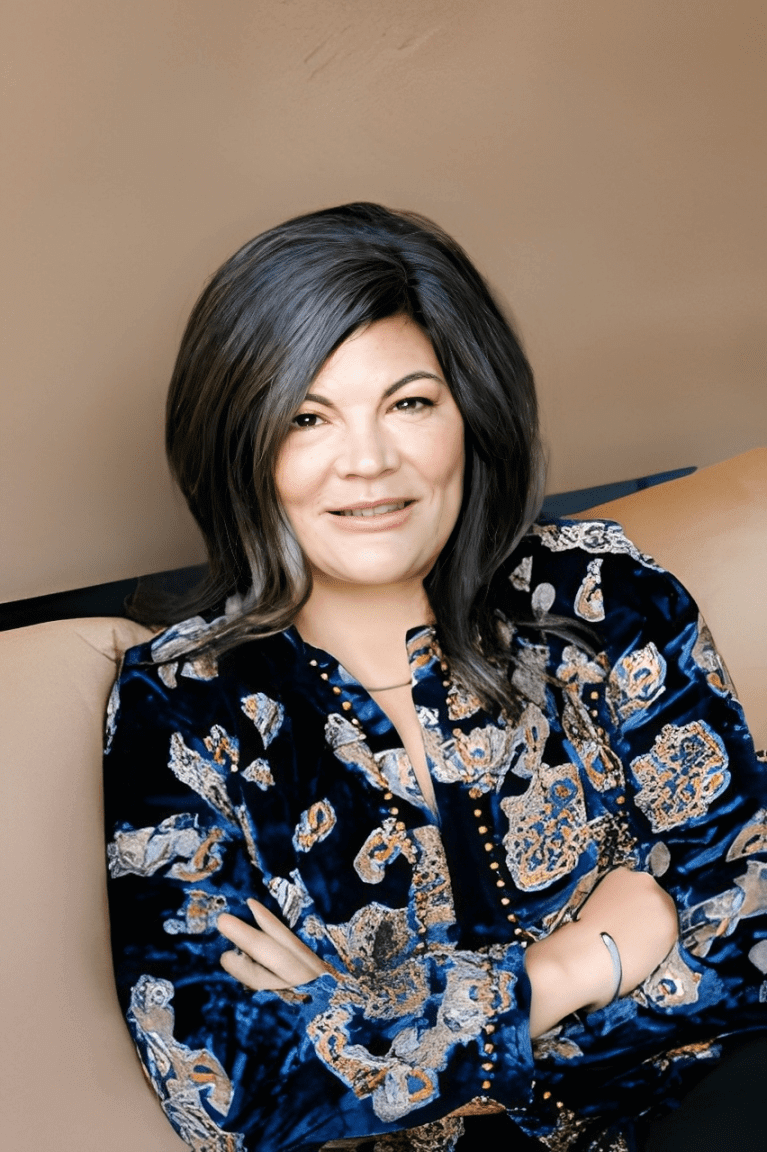 Woman smiling in patterned blue blouse.